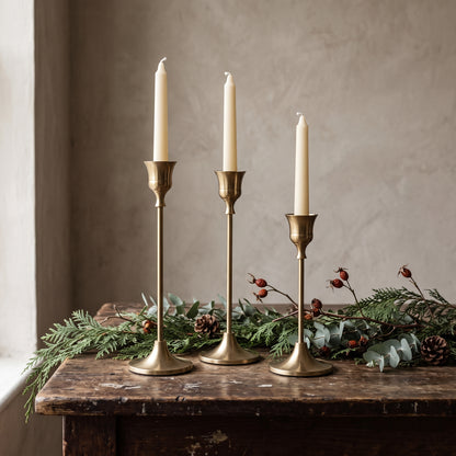 Gold taper candle holders in three heights on a rustic wooden table